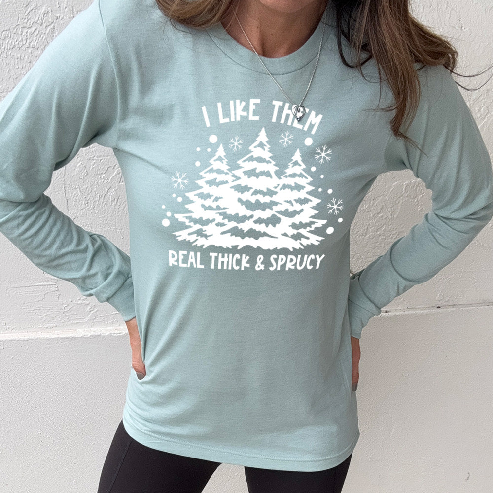 heather dusty blue long sleeve with the words "I like them real thick & sprucy" and the graphics of big christmas trees and smaller snowflakes
