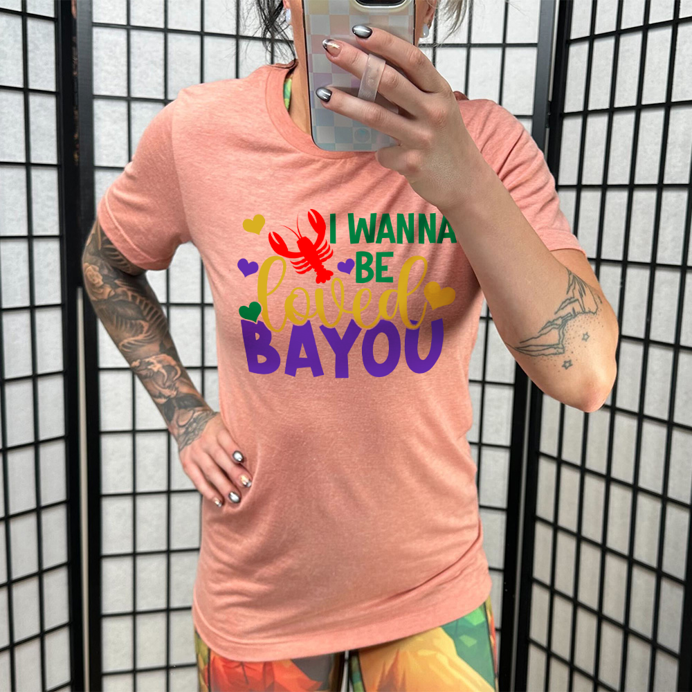 sunset unisex tee with the words "I wanna be loved bayou" on it in varied fonts, with the small graphics a few hearts and one lobster
