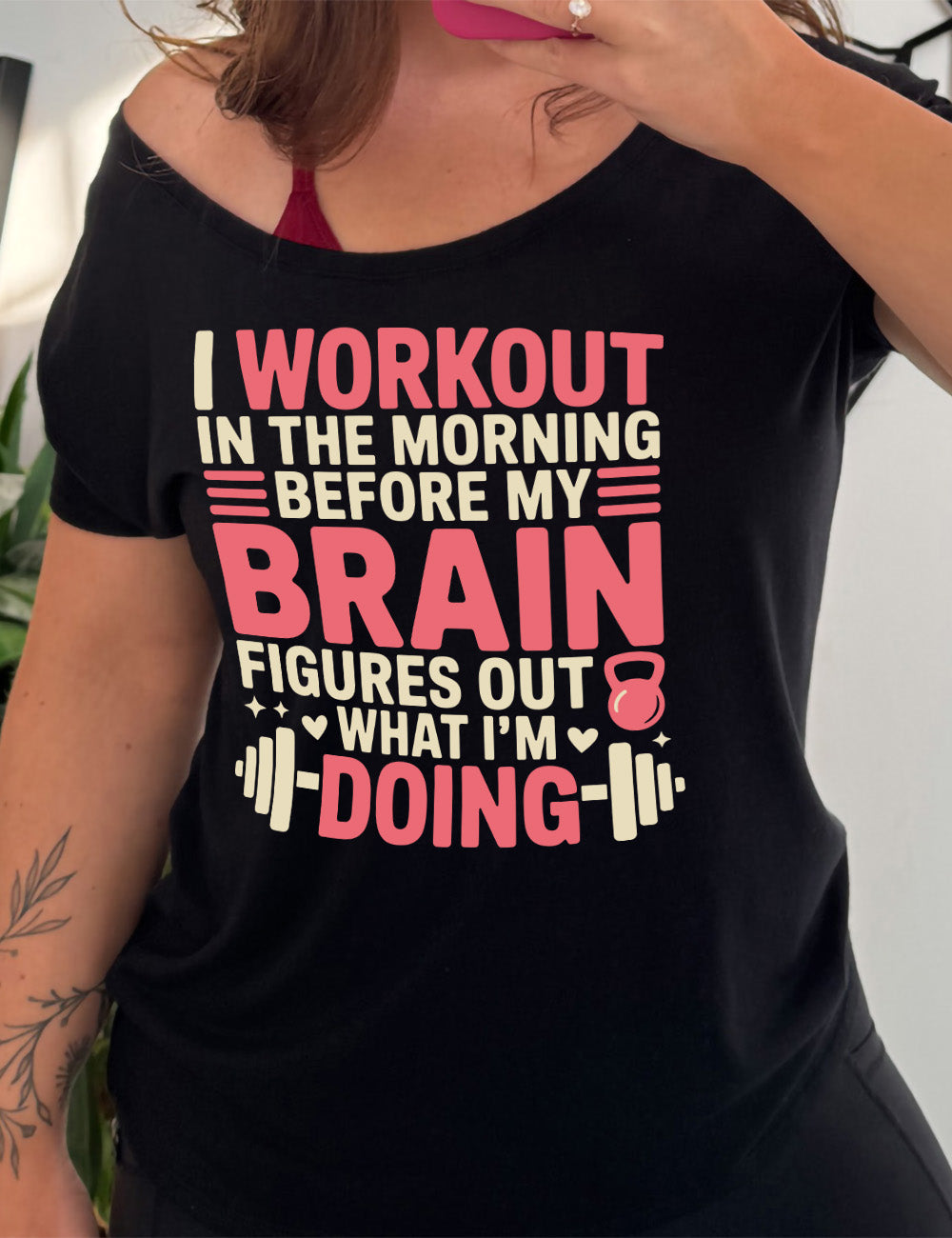 black slouchy tee with words on it saying "I workout in the morning before my brain figures out what I'm doing", with the graphics of lines, a kettlebell, a couple stars and hearts, and a barbell