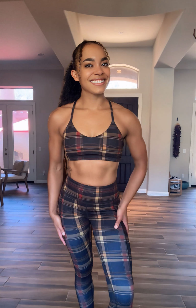 A woman modeling a matching plaid activewear set consisting of a sports bra and high-waisted leggings