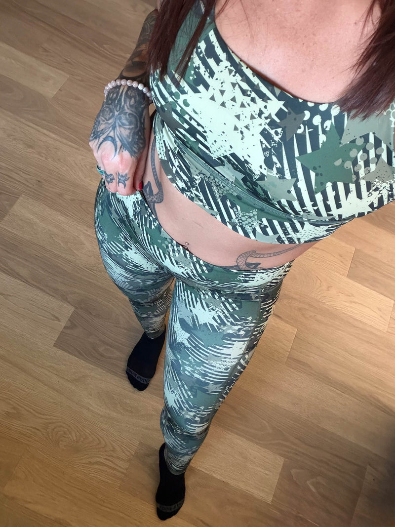 A person wearing a matching activewear set with a green and white camouflage pattern, standing on a light wood floor.