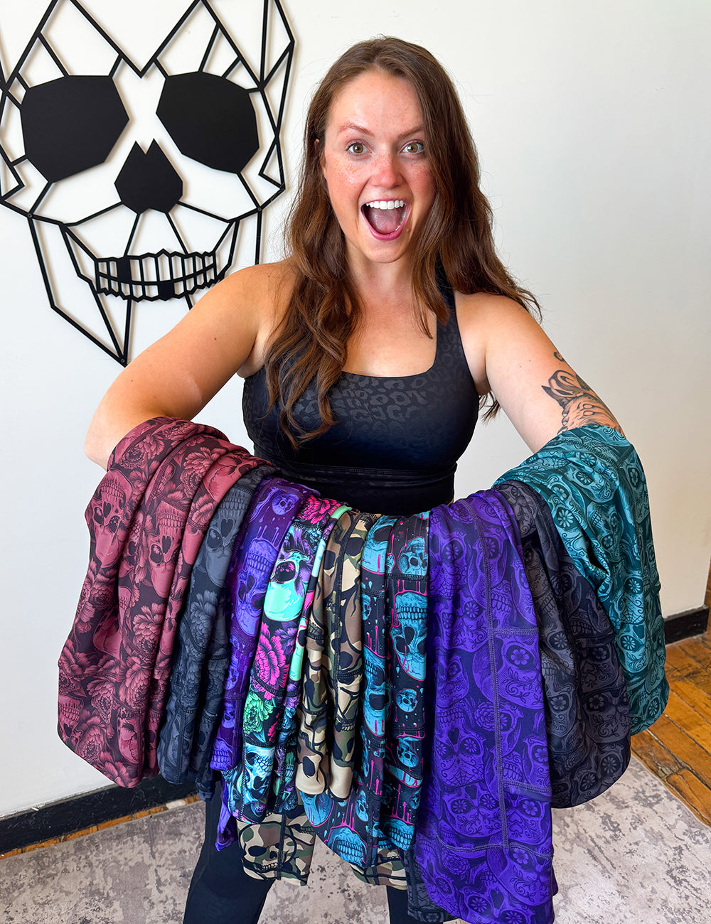Model holding all 9 of the new skull sealed series on her arm, against a geometric skull background