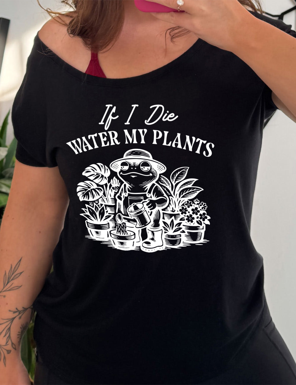 black slouchy tee with the words "If I die water my plants" on it, and underneath a graphic of a contented frog in a gardening outfit, watering a plant, surrounded by other plants