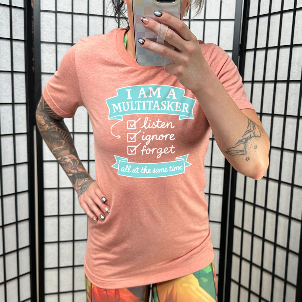 Sunset Unisex Tee, with wording I am a Multitasker listen ignore forget all at the same time, checkmarks, an arrow, and banners