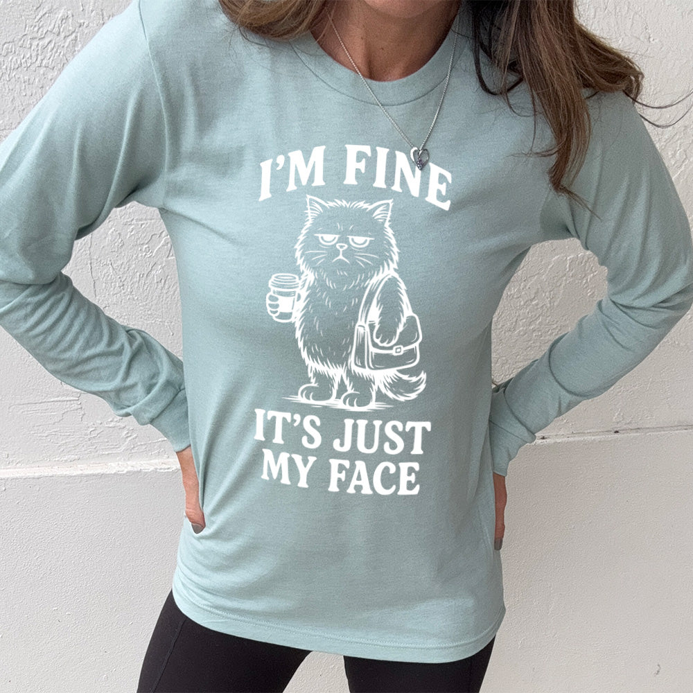heather dusty blue long sleeve shirt with the words "I'm fine it's just my face" on it, around the graphic of a cat with a resting-grumpy face, holding a coffee and wearing a purse