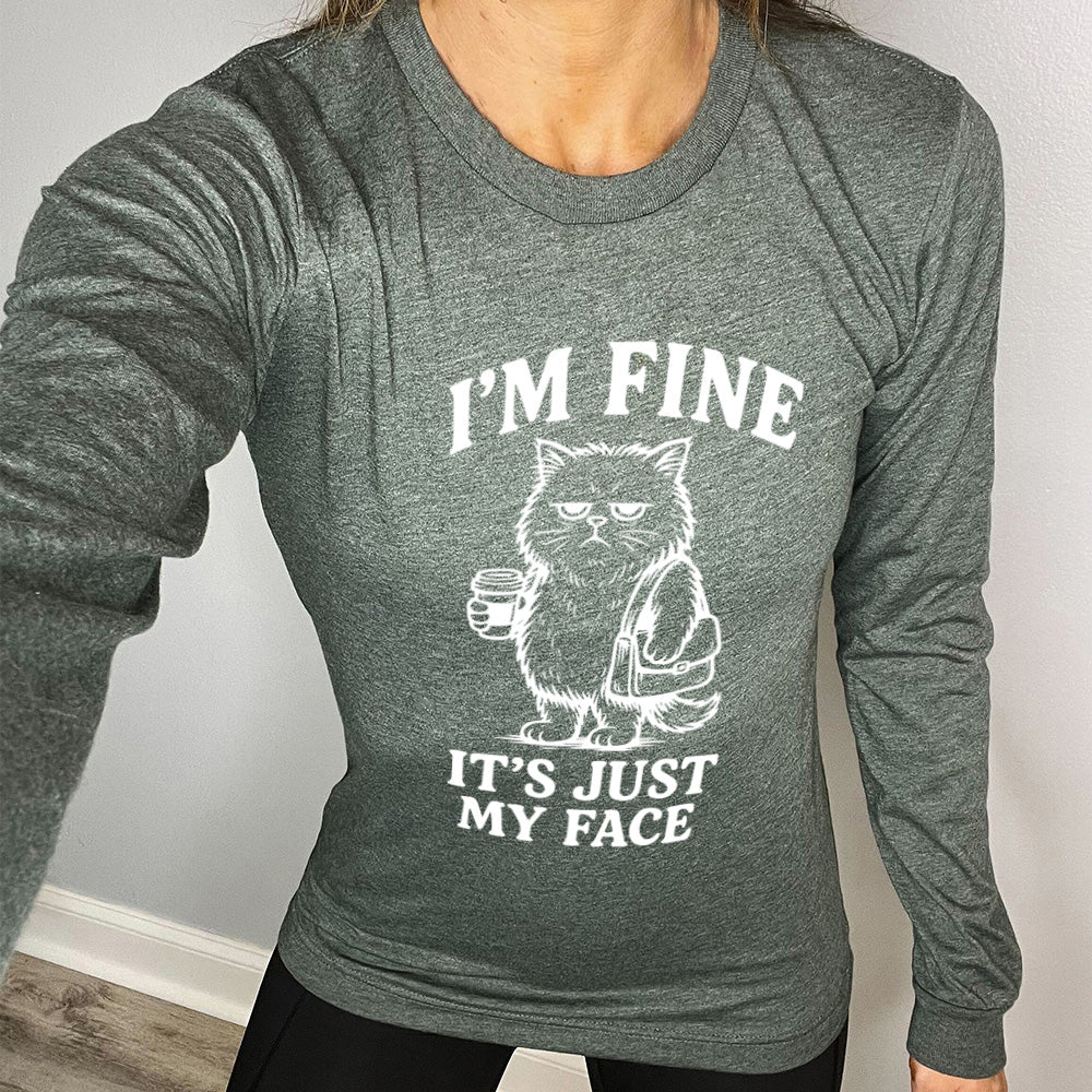 heather forest long sleeve shirt with the words "I'm fine it's just my face" on it, around the graphic of a cat with a resting-grumpy face, holding a coffee and wearing a purse