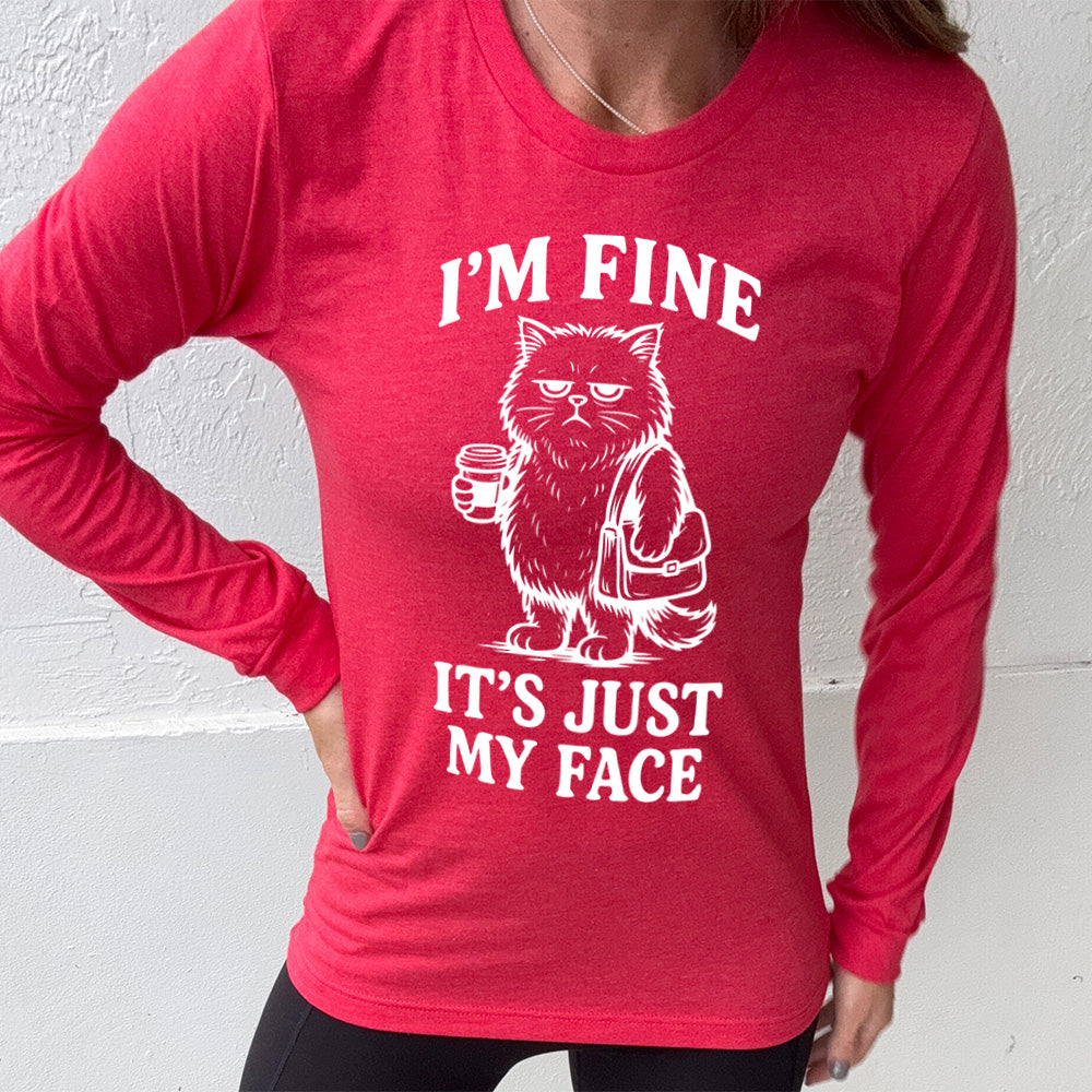 heather red long sleeve shirt with the words "I'm fine it's just my face" on it, around the graphic of a cat with a resting-grumpy face, holding a coffee and wearing a purse