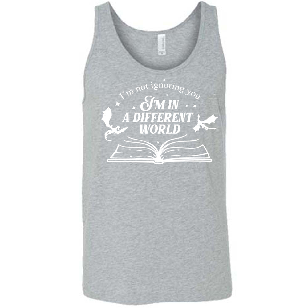 grey unisex tank with the words "I'm not ignoring you I'm in a different world" on it, with the graphic of a large book, lying open, and two little dragons flying next to the words, a few stars scattered around
