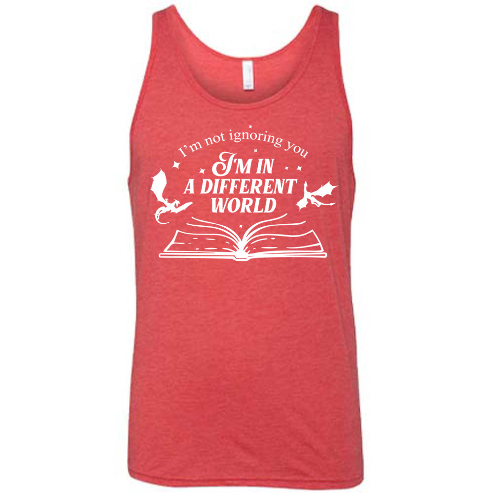 red unisex tank with the words "I'm not ignoring you I'm in a different world" on it, with the graphic of a large book, lying open, and two little dragons flying next to the words, a few stars scattered around