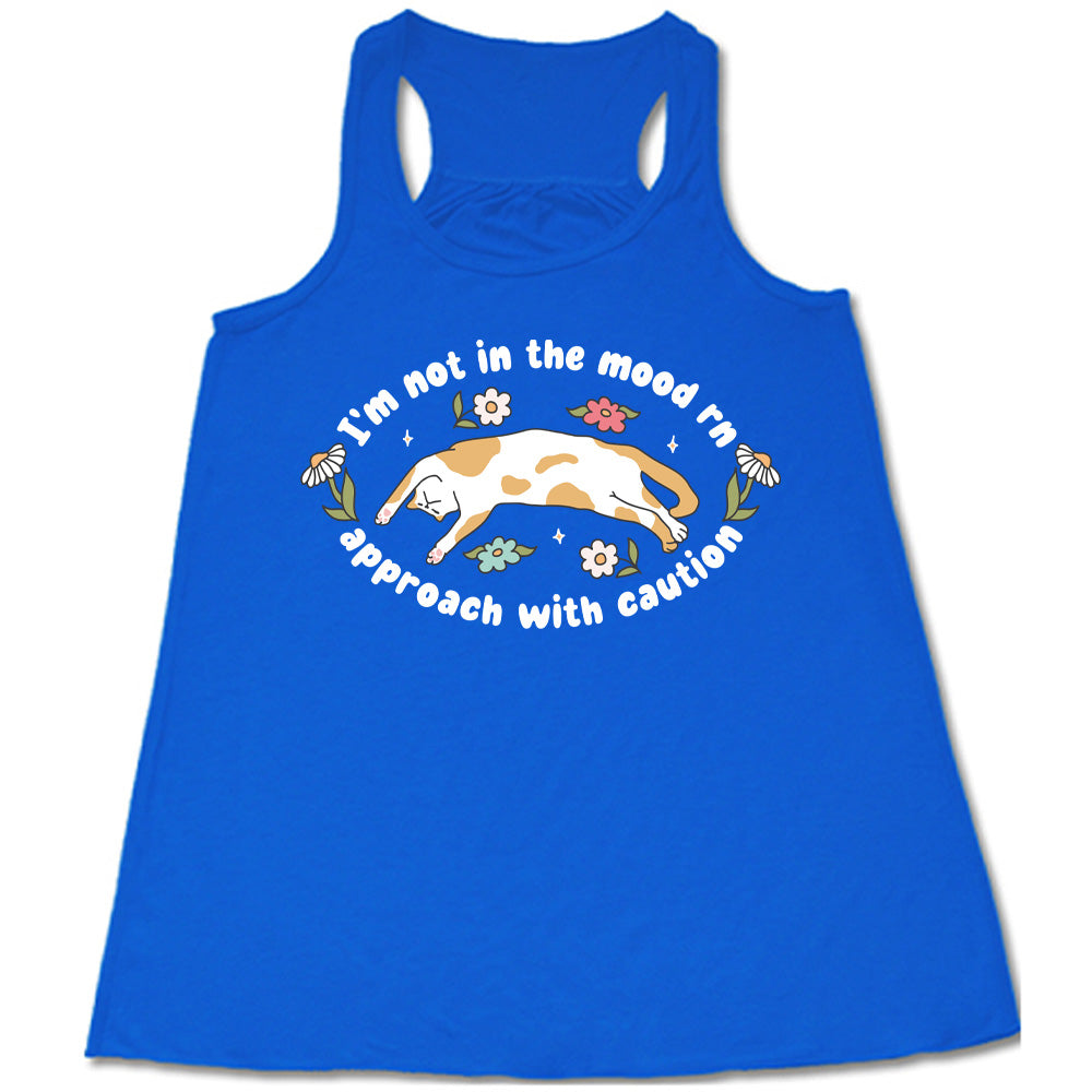 blue racerback tank with the words "I'm not in the mood rn approach with caution" on it in an oval, with the graphic of a cat splayed on its back within the words, and a few flowers around