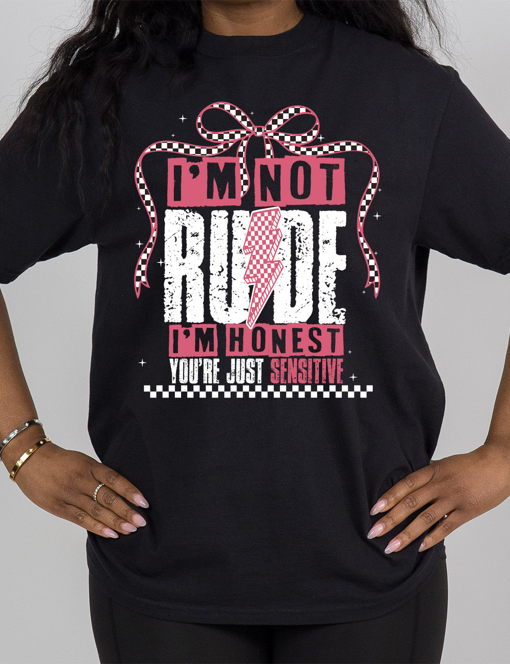 black modern tee with print placement on the front, in punk style, with the words "I'm not rude I'm honest you're just sensitive" on it, with a checkered lightning bolt in the middle of the word "rude" and a checkered bow arching over the words, and a checkered band below them, and a few small stars scattered around