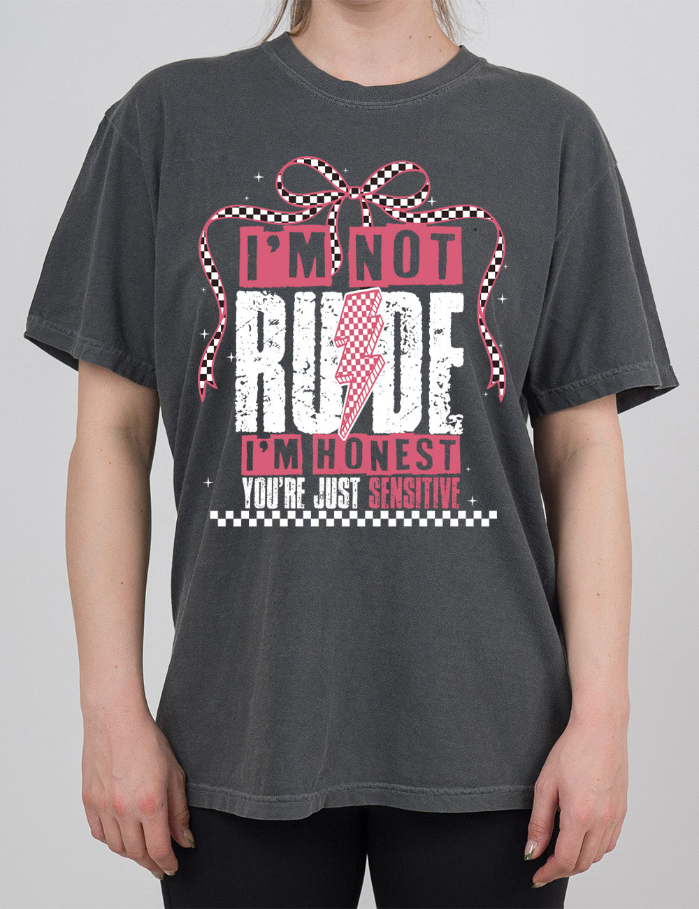 pepper modern tee with print placement on the front, in punk style, with the words "I'm not rude I'm honest you're just sensitive" on it, with a checkered lightning bolt in the middle of the word "rude" and a checkered bow arching over the words, and a checkered band below them, and a few small stars scattered around