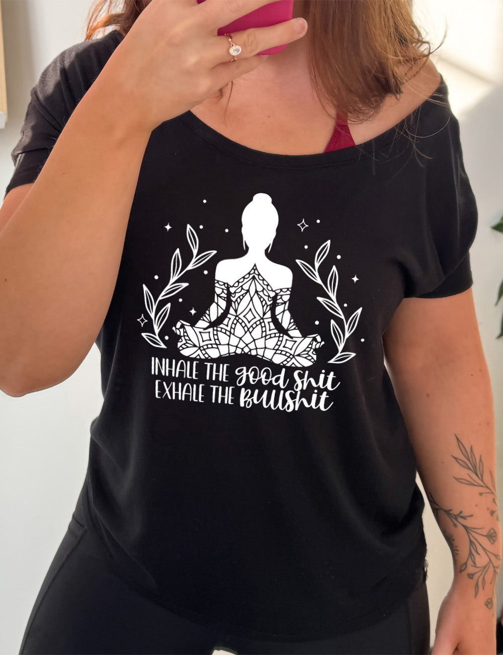 black slouchy tee with the graphic of a woman's silhouette (partially covered in elaborate shapes) with a plant on either side, surrounded by little stars, and the words underneath saying "Inhale the good shit exhale the bullshit"