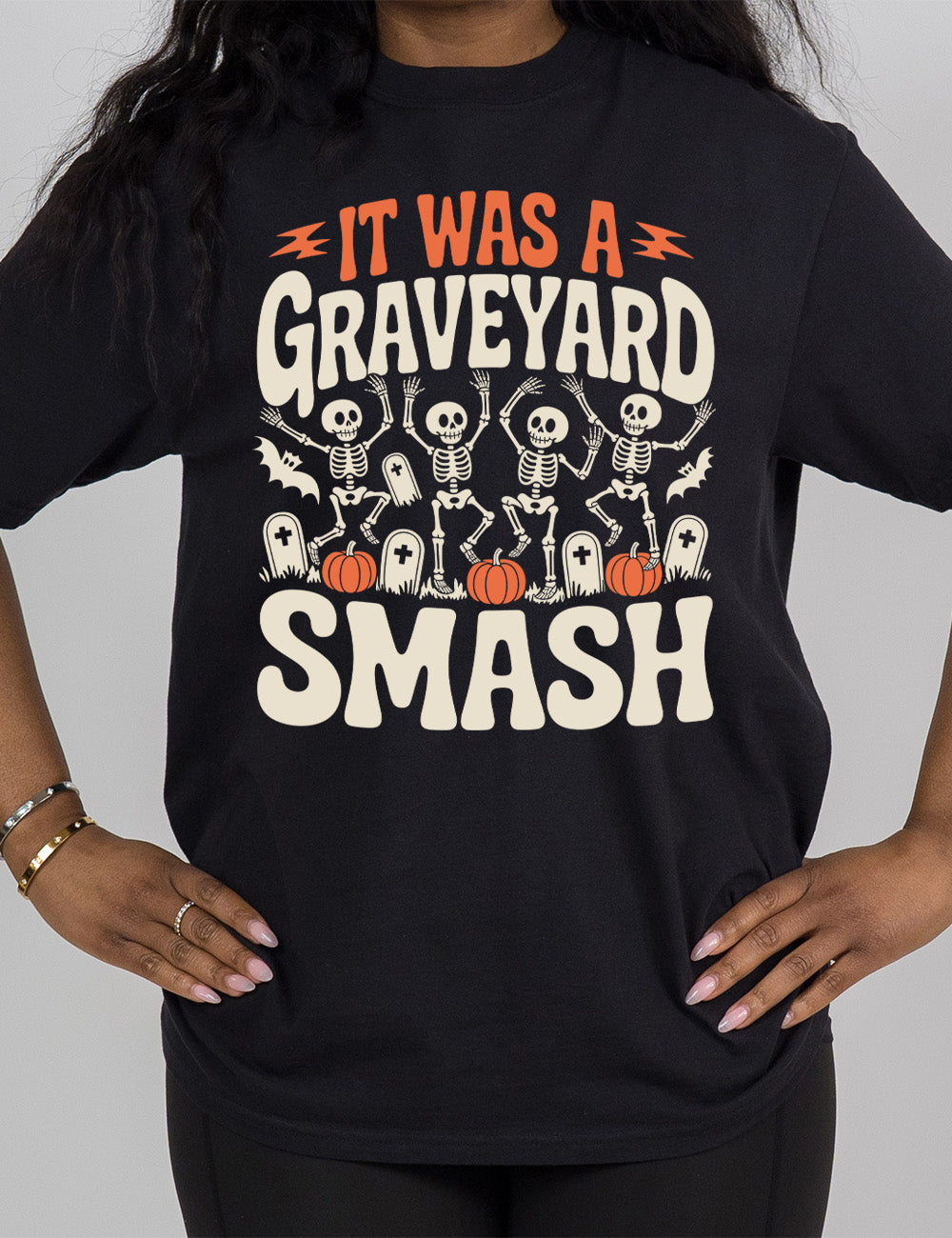 black modern tee with the words "it was a graveyard smash" with a lightning bolt on either side of the words "it was a" and the large graphic in the middle of the words of four skeletons dancing next to tombstones, pumpkins, and two bats