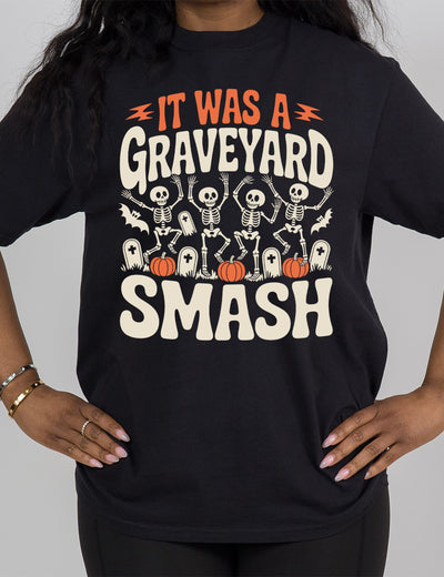 black modern tee with the words "it was a graveyard smash" with a lightning bolt on either side of the words "it was a" and the large graphic in the middle of the words of four skeletons dancing next to tombstones, pumpkins, and two bats