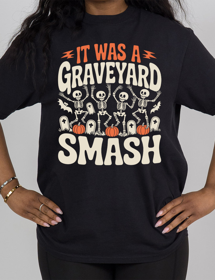 black modern tee with the words "it was a graveyard smash" with a lightning bolt on either side of the words "it was a" and the large graphic in the middle of the words of four skeletons dancing next to tombstones, pumpkins, and two bats