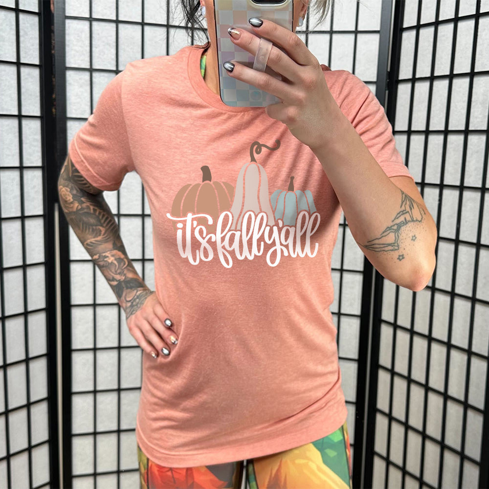 Model wearing sunset colored shirt with pumpkin and gourd graphic on it that says "It's Fall Y'all" 