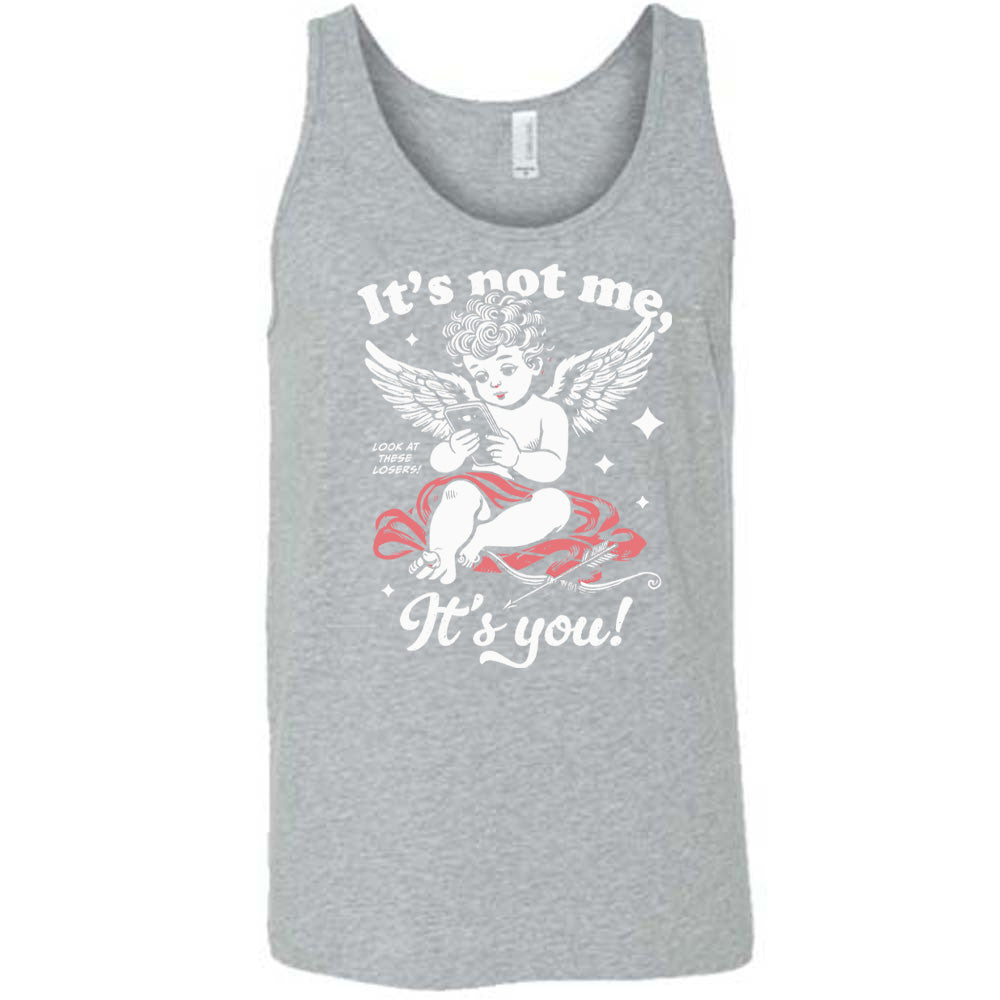 grey unisex tank with the words "it's not me, it's you!" on it, with graphics of Cupid looking at a cell phone (presumably looking at dating apps), with small words saying "look at these losers!" and Cupid's bow and arrow at his side