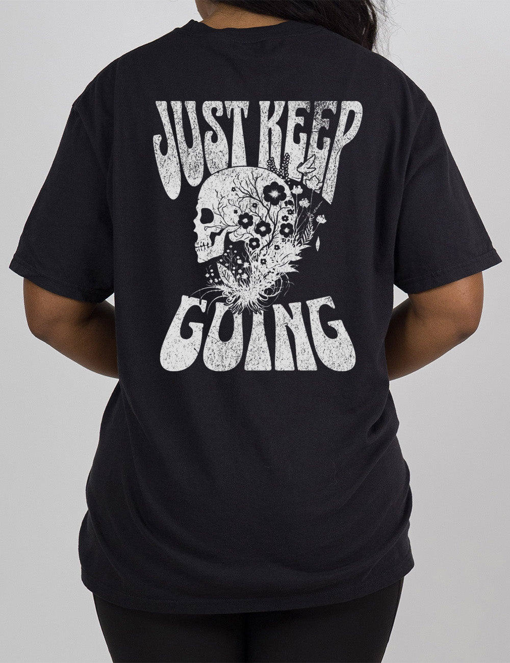 black modern tee with print placement on the back, with the words "just keep going" on it, with the graphic of a skull's profile, growing among plants