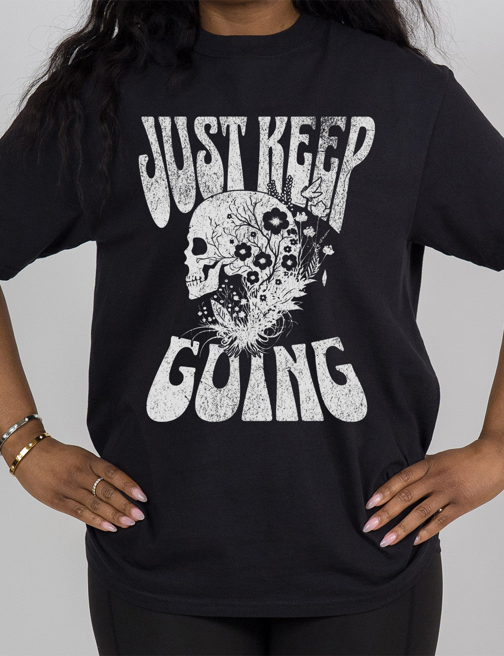 black modern tee with print placement on the front, with the words "just keep going" on it, with the graphic of a skull's profile, growing among plants