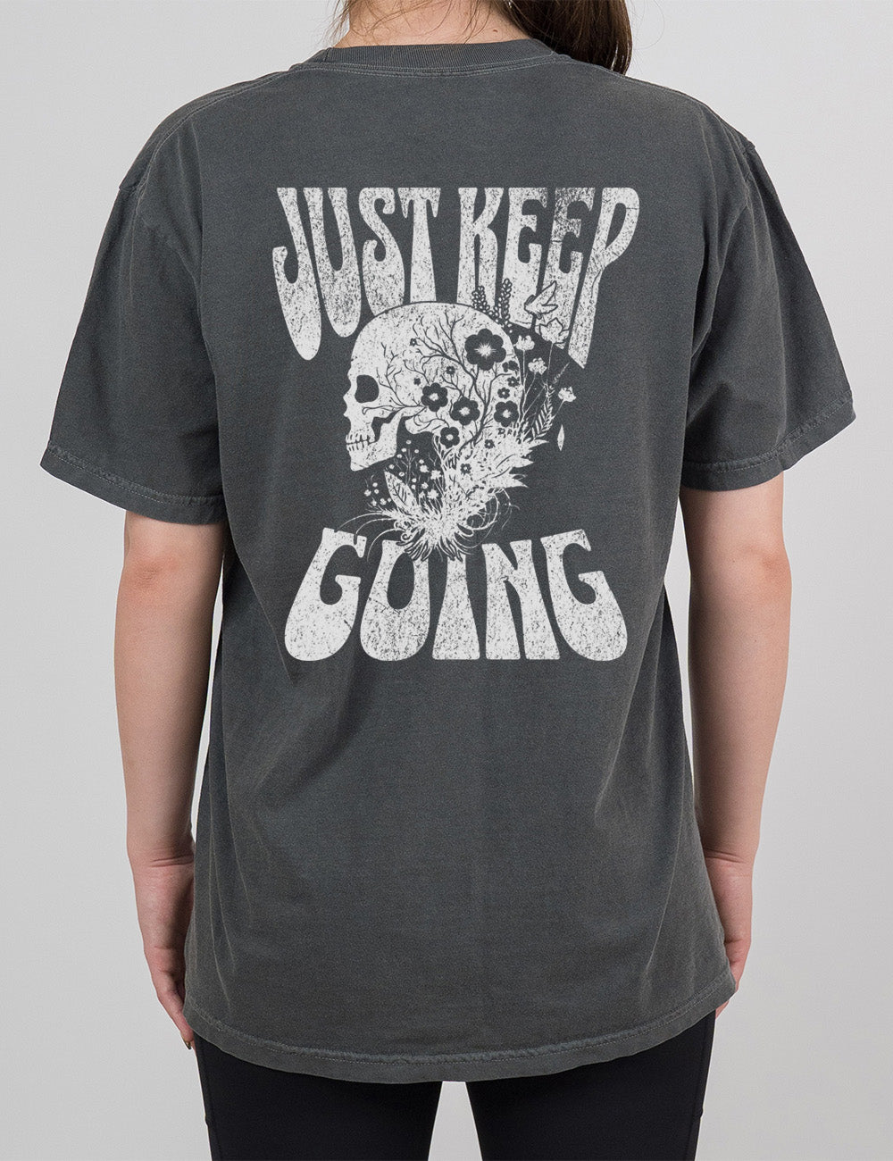 pepper modern tee with print placement on the back, with the words "just keep going" on it, with the graphic of a skull's profile, growing among plants