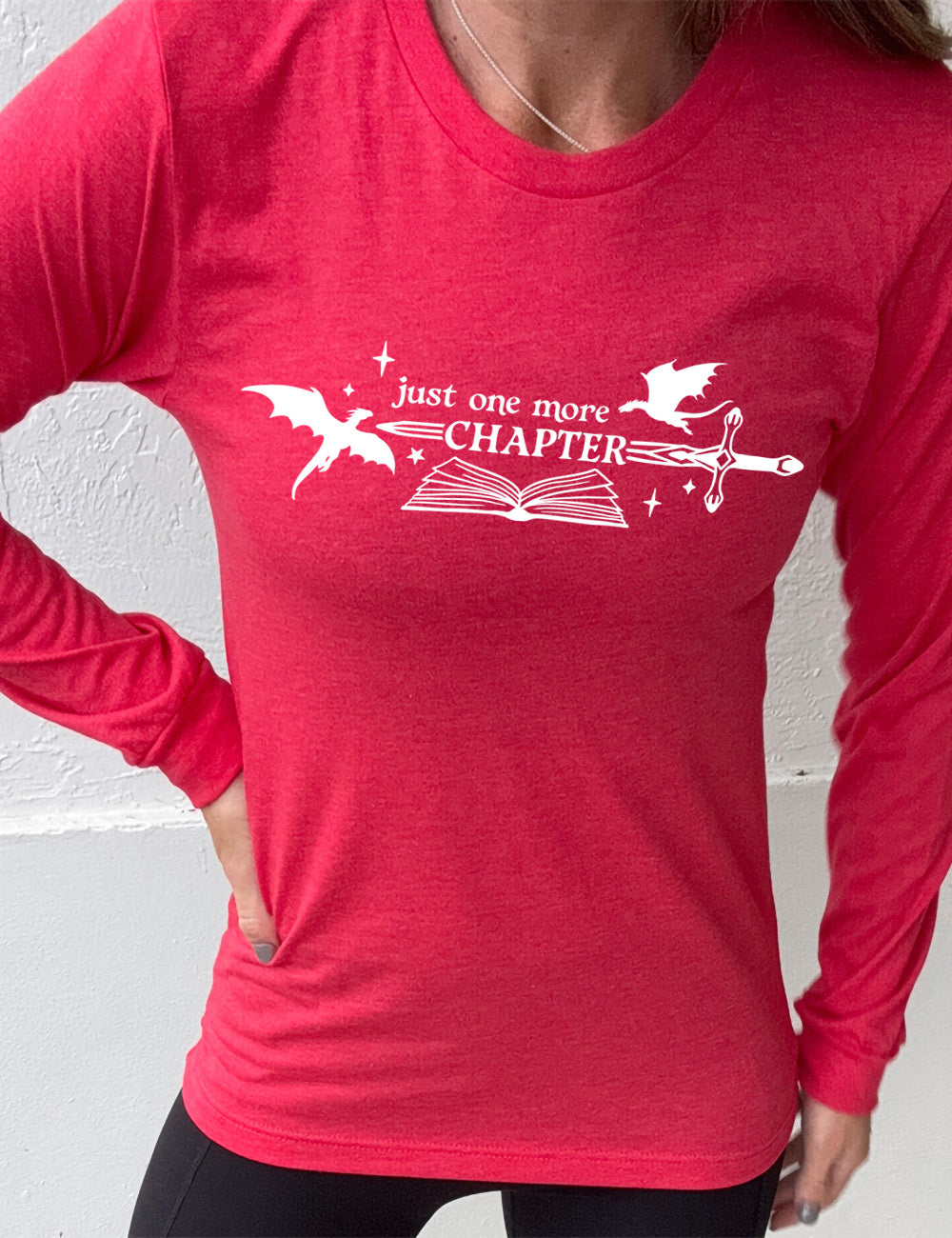 heather red long sleeve shirt with the graphic of an open book, with stars and a couple dragon silhouettes, and a sword, and the words "just one more chapter" on it, with the word "chapter" overlaying the sword