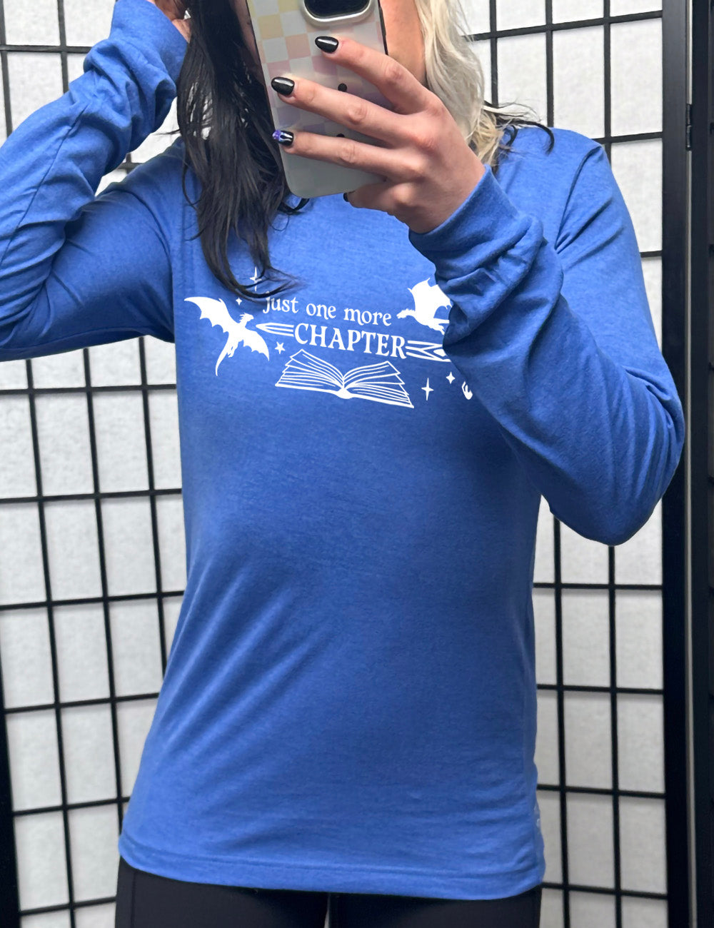 heather true royal long sleeve shirt with the graphic of an open book, with stars and a couple dragon silhouettes, and a sword, and the words "just one more chapter" on it, with the word "chapter" overlaying the sword