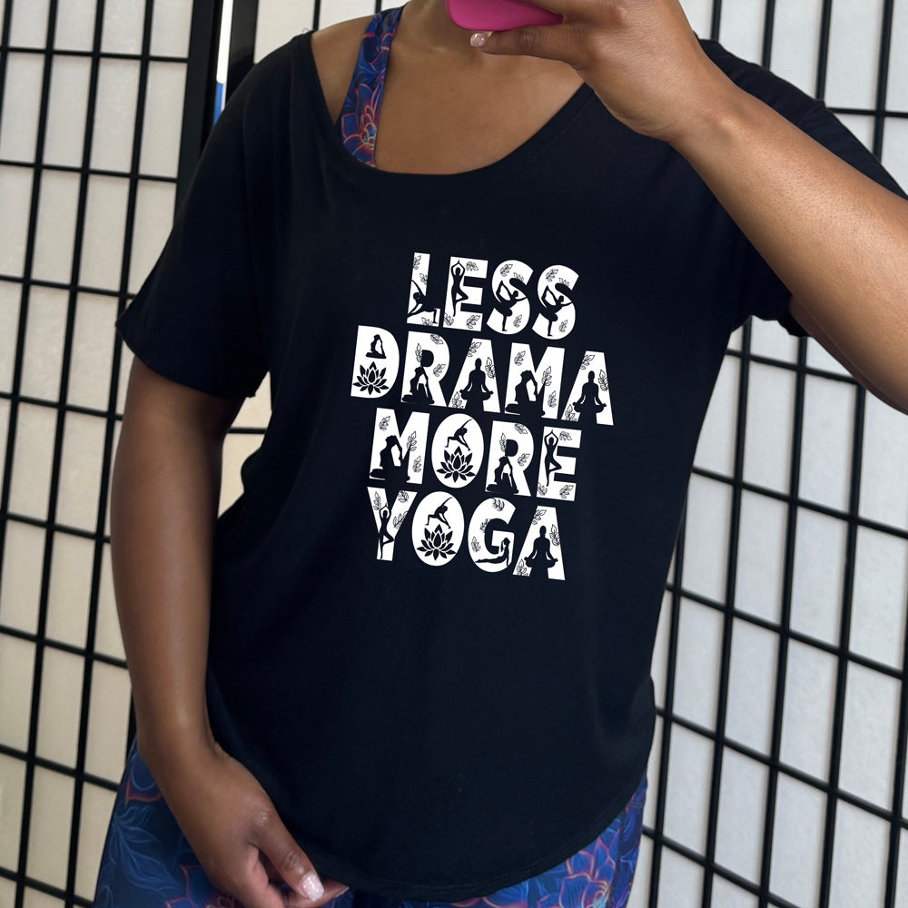 black slouchy shirt  with the words "less drama more yoga" on it, and within each letter there are silhouettes of people doing yoga poses as well as some lotus flowers and some leaves