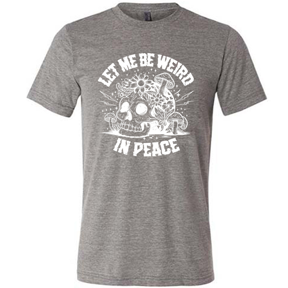grey unisex tee with the words "let me be weird in peace" on it with the graphic of a skull on the ground with mushrooms growing on and around it, as well as flowers growing on it, surrounded by little stars and lightening bolts