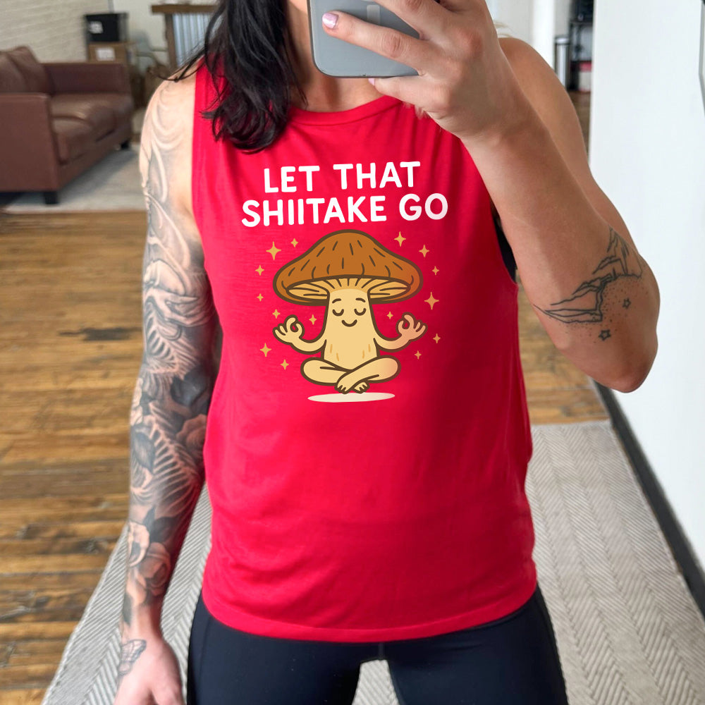 red muscle tank with the words "let that shiitake go" on it and the graphic of a mushroom doing a yoga pose, surrounded by little stars
