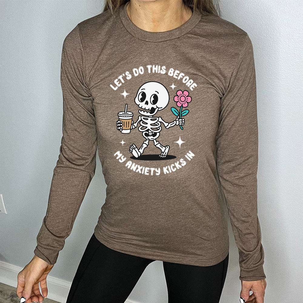 heather brown long sleeve shirt with the text "Lets Do This Before My Anxiety Kicks In" on it, and the graphic of a cartoon skeleton walking with a flower in one hand and a drink in the other