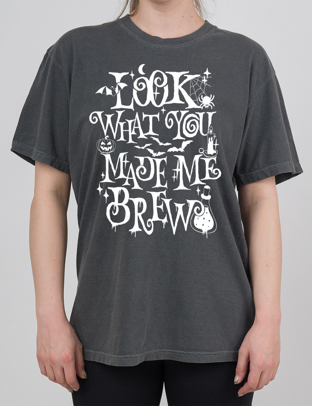 pepper modern tee with the curly, dripping words saying "look what you made me brew" (with the "o" being a spiral) and the graphics of a potion, a spider in its web, a candle, a bat some bats, stars, and a jack-o-lantern