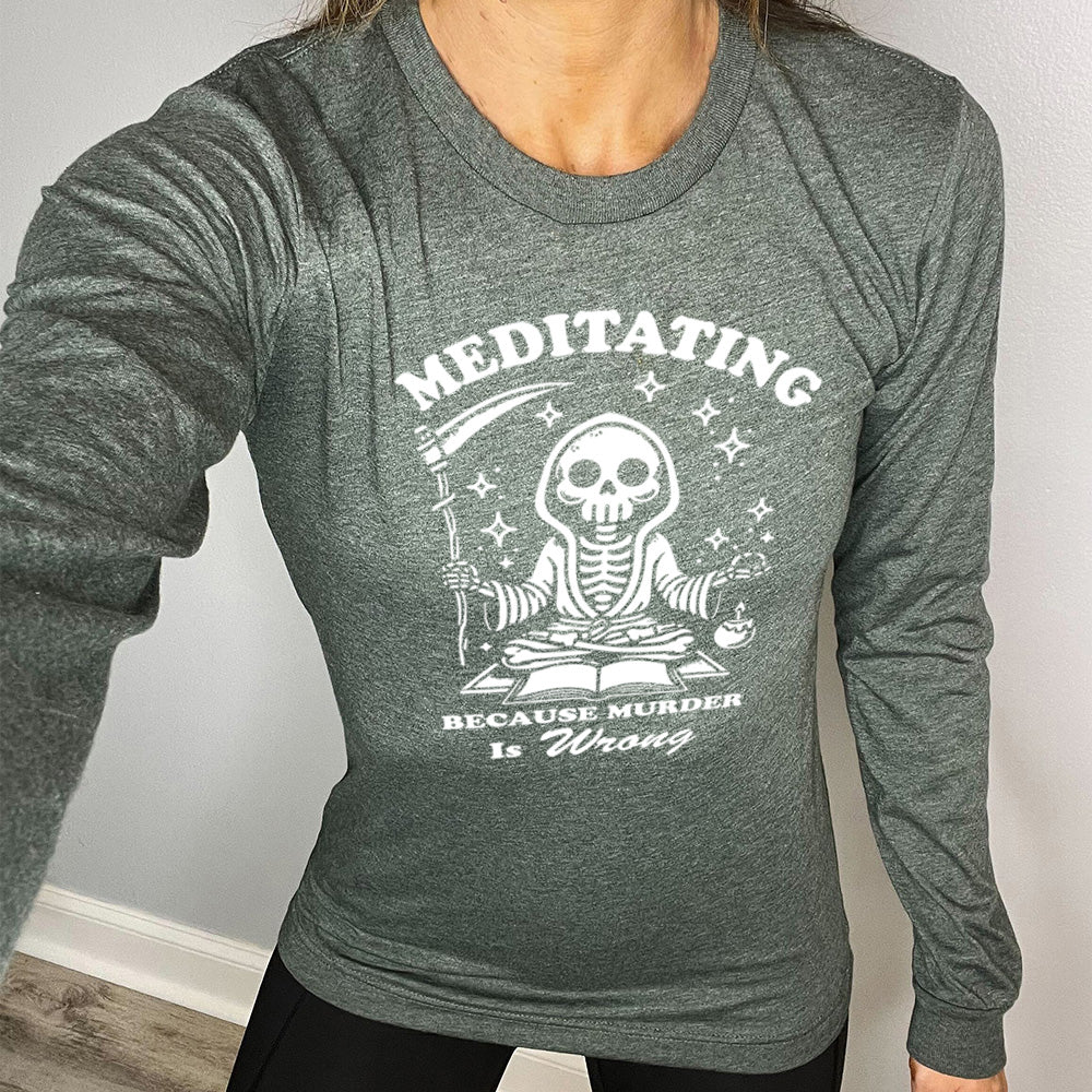 heather forest long sleeve shirt with the text "Meditating Because Murder is Wrong" on it, with the graphic of a skeleton wearing a robe, holding a scythe, and meditating in front of an open book, with a little candle beside, and little stars scattered around