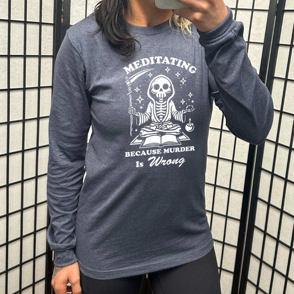 heather navy long sleeve shirt with the text "Meditating Because Murder is Wrong" on it, with the graphic of a skeleton wearing a robe, holding a scythe, and meditating in front of an open book, with a little candle beside, and little stars scattered around