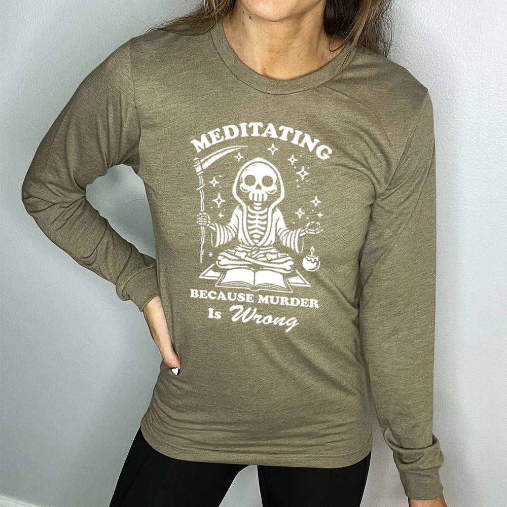 heather olive long sleeve shirt with the text "Meditating Because Murder is Wrong" on it, with the graphic of a skeleton wearing a robe, holding a scythe, and meditating in front of an open book, with a little candle beside, and little stars scattered around