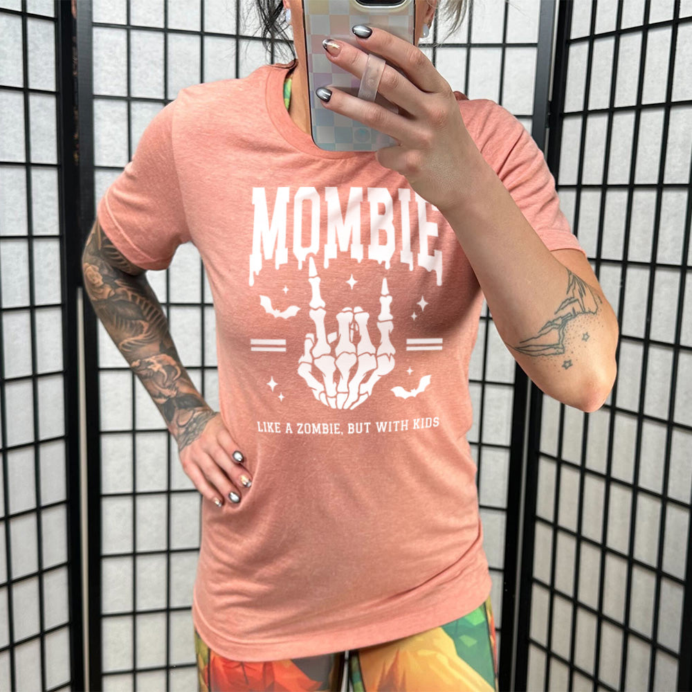 sunset unisex tee with the big word "mombie" on it, with the graphic of a skeletal hand giving the rocker sign, with a couple bats and a number of little stars, and two equal signs, with small words underneath it all saying "like a zombie, but with kids"