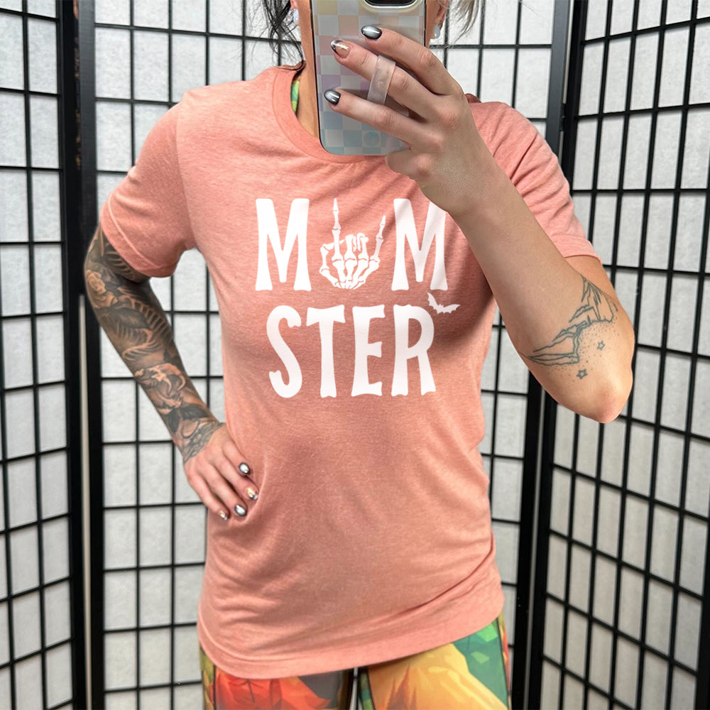 sunset unisex tee with the word "momster" on it, with the "o" of the word being the graphic of a skeletal rocker hand, and one little bat after the word