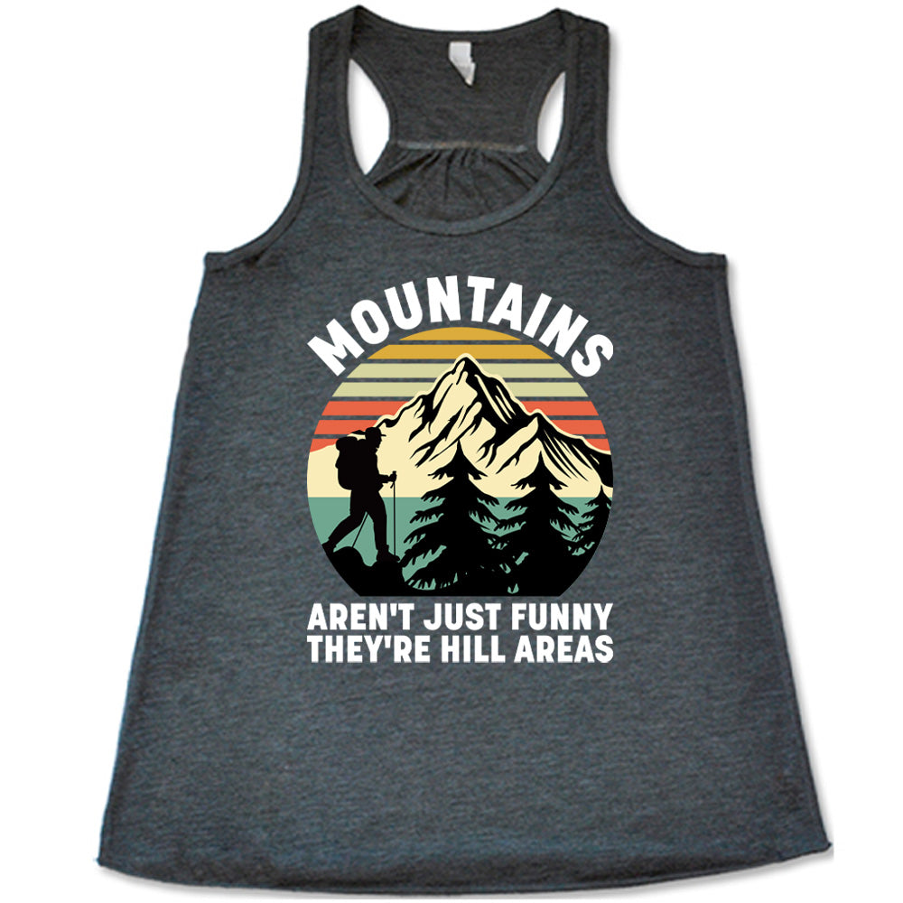 grey flowy tank with the words "mountains aren't just funny they're hill areas" on it, with the graphic of a mountain, trees, a colorful sky, and the silhouette of a hiker