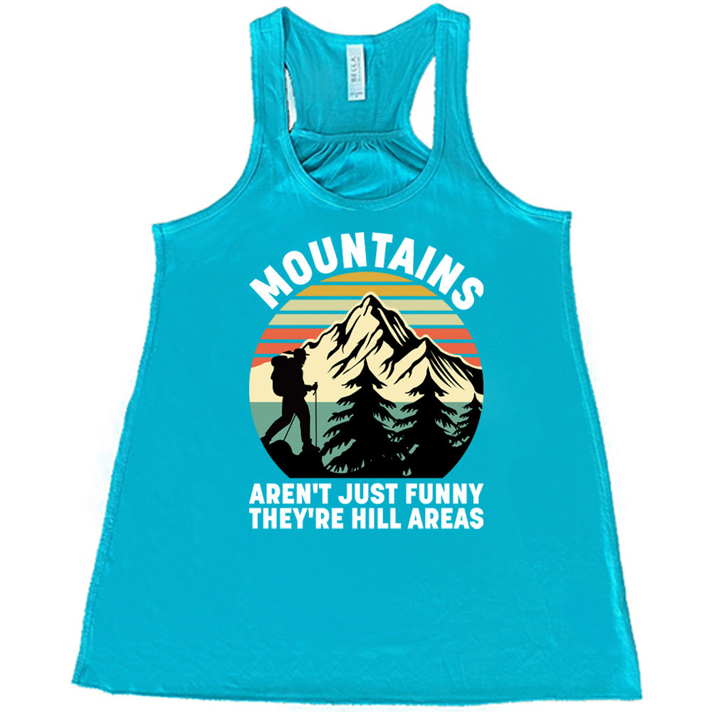 teal flowy tank with the words "mountains aren't just funny they're hill areas" on it, with the graphic of a mountain, trees, a colorful sky, and the silhouette of a hiker