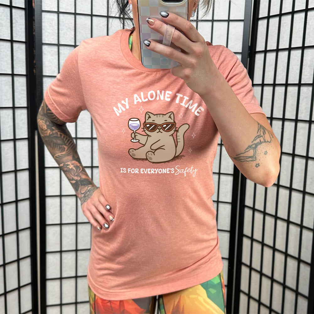 Model wearing sunset colored shirt with a cat holding a wine glass graphic on it that says "My Alone Time Is For Everyone's Safety" 