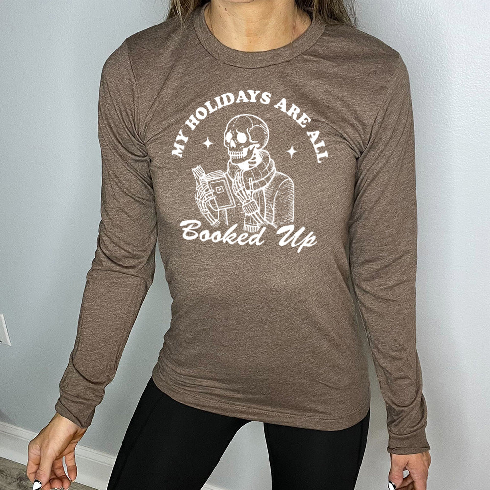 heather brown long sleeve with the words "my holidays are all booked up", with the image of a skeleton dressed warmly and reading a book