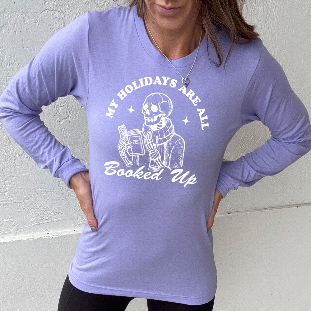 heather dark lavender long sleeve with the words "my holidays are all booked up", with the image of a skeleton dressed warmly and reading a book