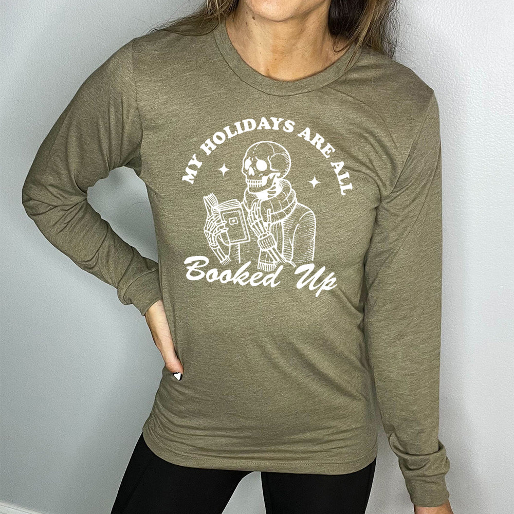 heather olive long sleeve with the words "my holidays are all booked up", with the image of a skeleton dressed warmly and reading a book