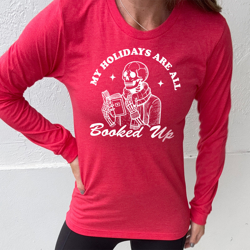 heather red long sleeve with the words "my holidays are all booked up", with the image of a skeleton dressed warmly and reading a book