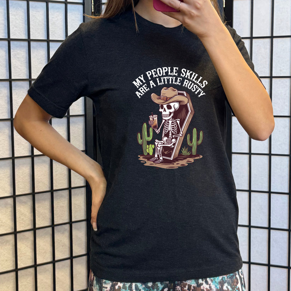 Black colored shirt with a skeleton sitting in a coffin graphic on it that says "My People Skills Are A Little Rusty" 