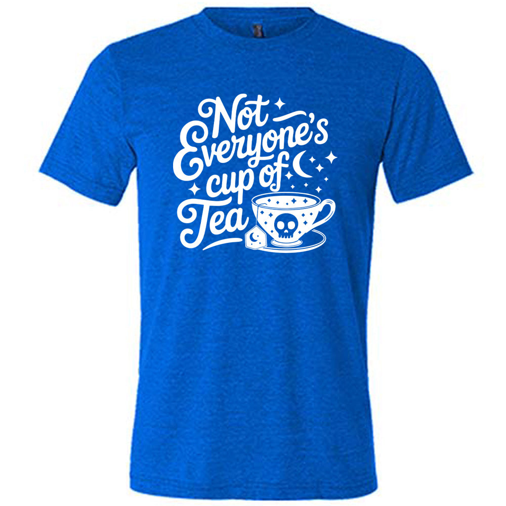 blue unisex tee with the words "not everyone's cup of a tea" in a cursive font, with the graphics of a moon and little stars, and a tea cup with a skull on it with stars and the tea bag has a moon on it