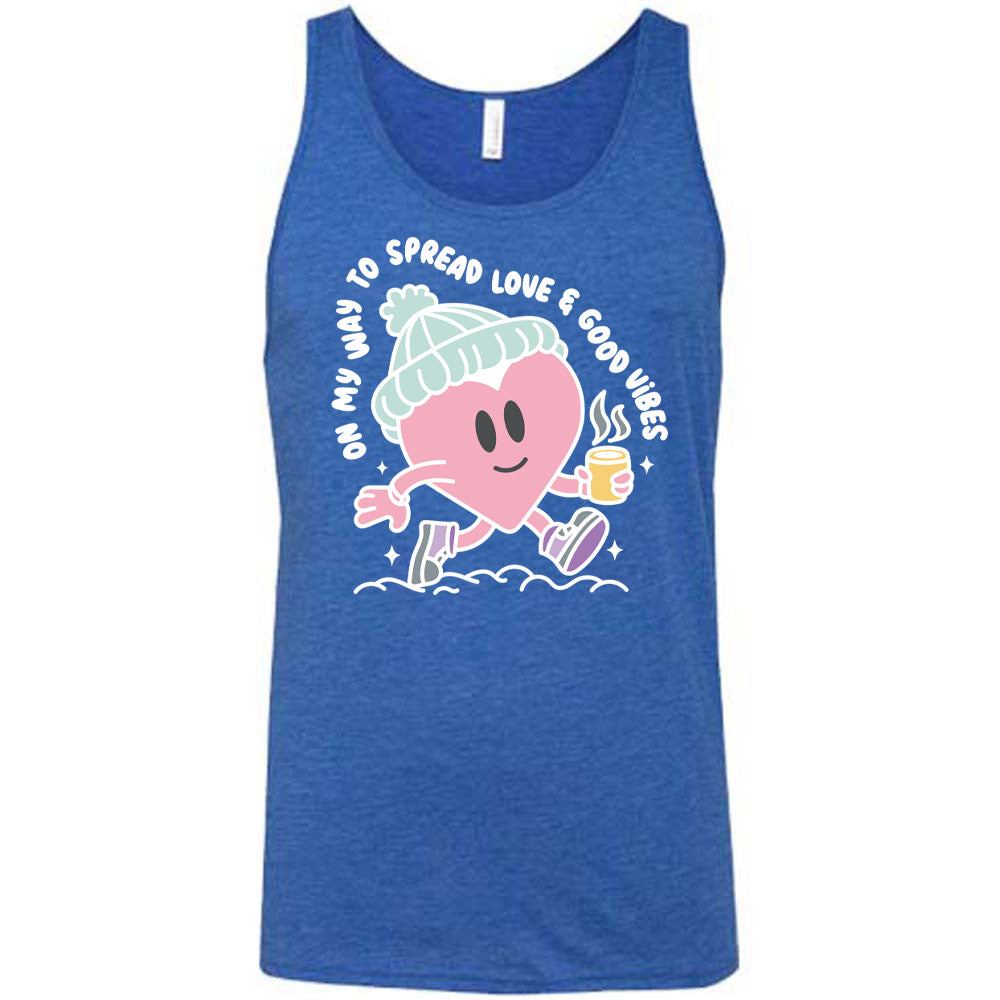 blue unisex tank with the words "on my way to spread love & good vibes" on it, with graphics of a cheerful, cartoony heart strolling along with a mug of a hot drink steaming in its hand, a hat on its head, and shoes on