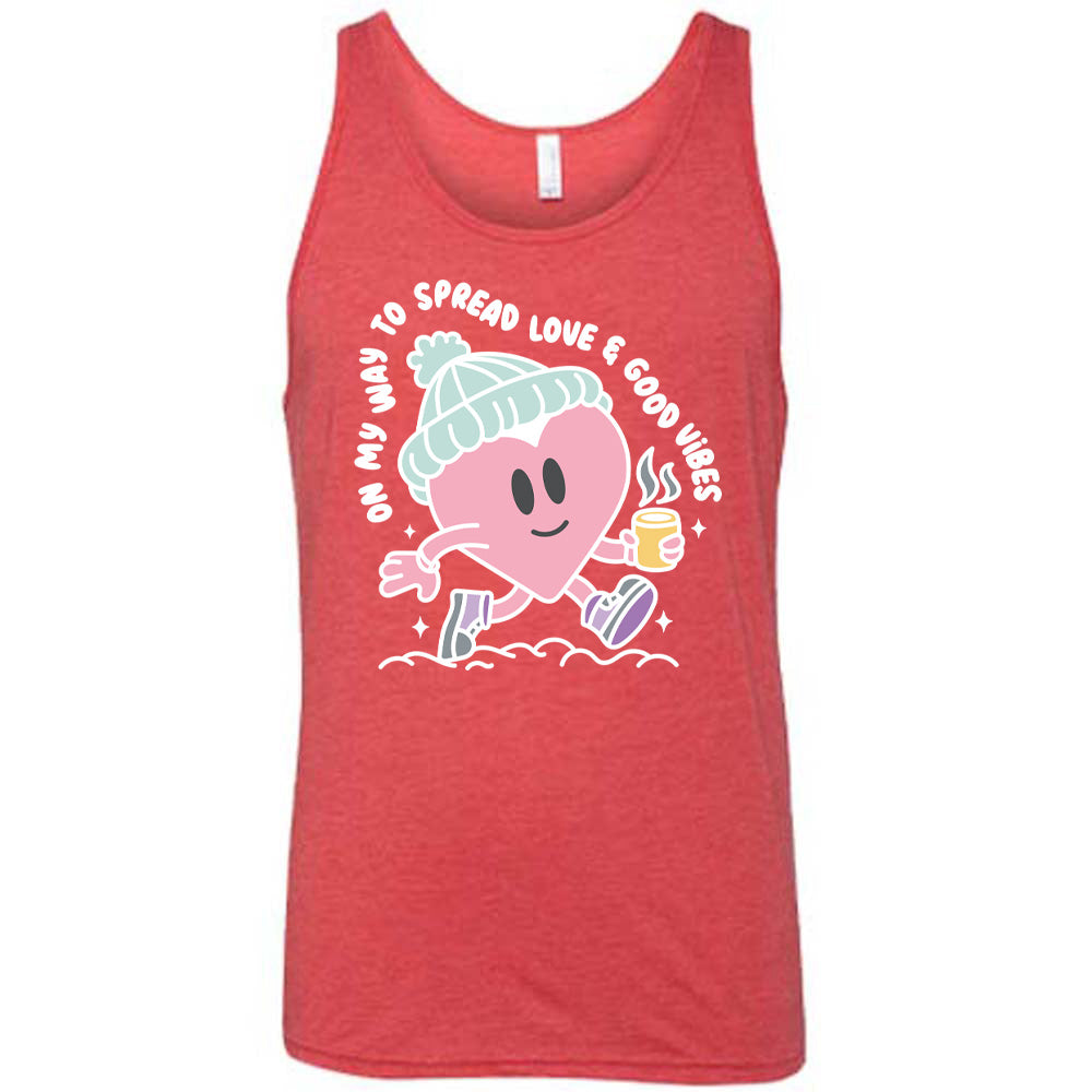 red unisex tank with the words "on my way to spread love & good vibes" on it, with graphics of a cheerful, cartoony heart strolling along with a mug of a hot drink steaming in its hand, a hat on its head, and shoes on