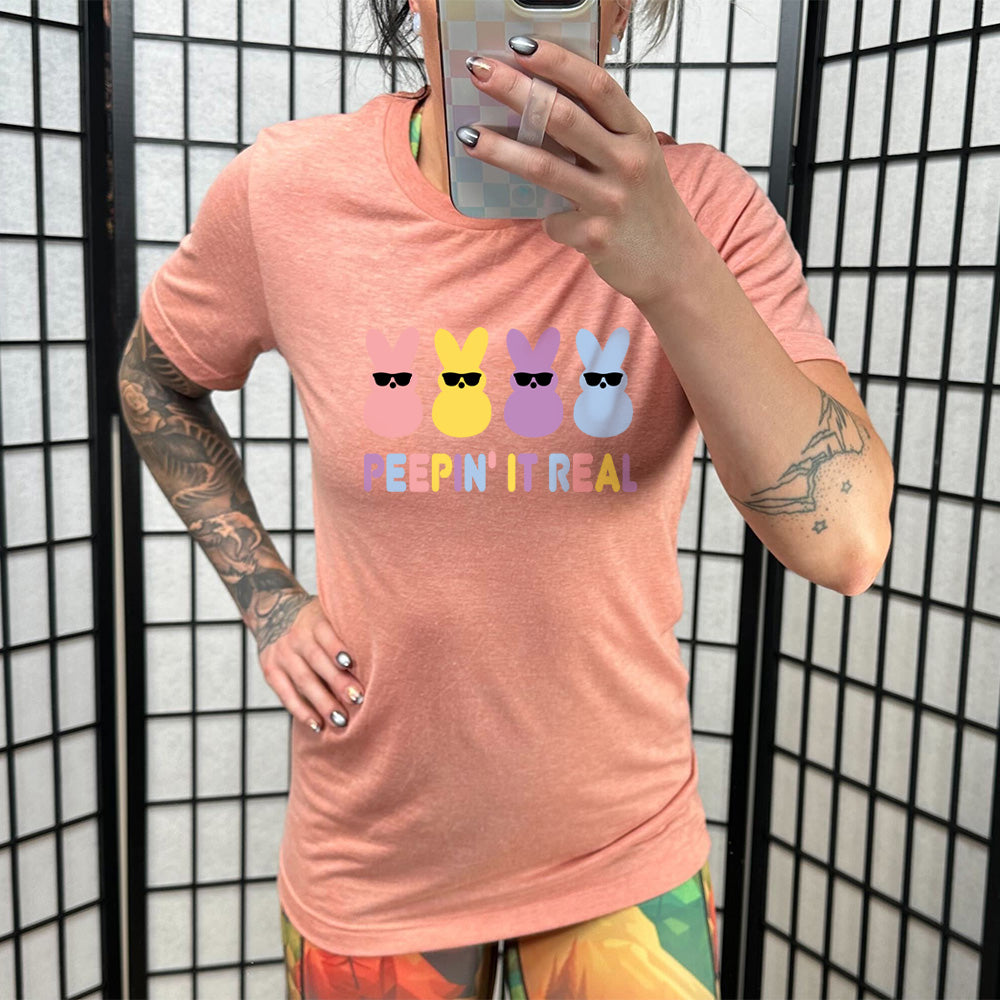 Sunset colored shirt with an Easter-colored bunnies graphic on it that says "Peepin it Real" 