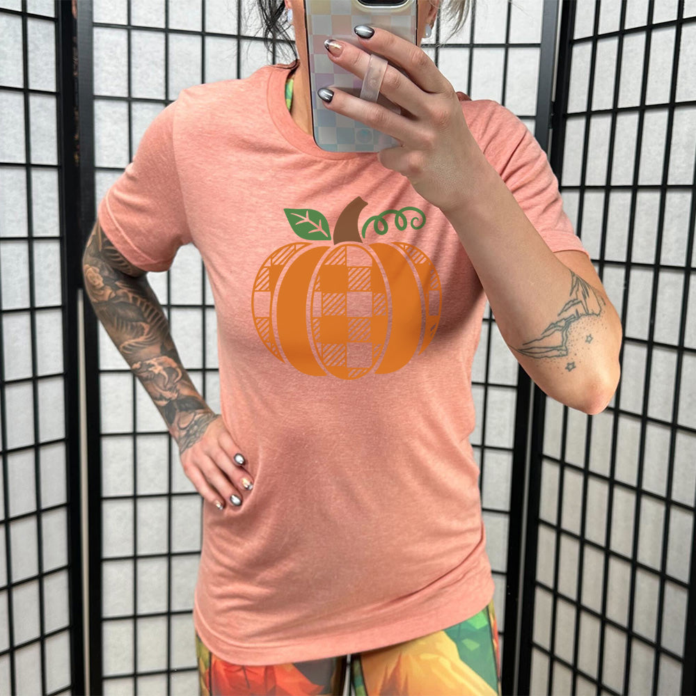 Model wearing sunset colored shirt with plaid pumpkin graphic on it